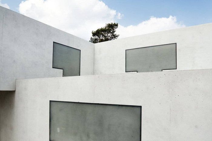 Corner of a building made from three intersecting blocks of concrete. Cut into them are darker grey shapes looking like Tetris blocks.