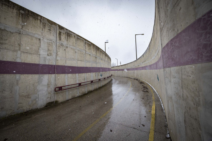 A curving rainslick road, flanked on both sides by grey concrete walls. 