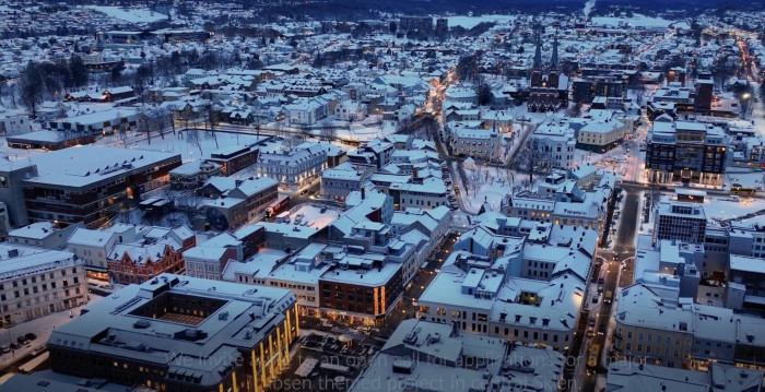 Aerial view of a town in Skien around dusk - snow-covered rooftops and streets lined with strings of yellow lights.