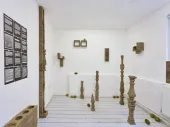 A gallery space with works on the walls and sculptural pieces in the middle. 