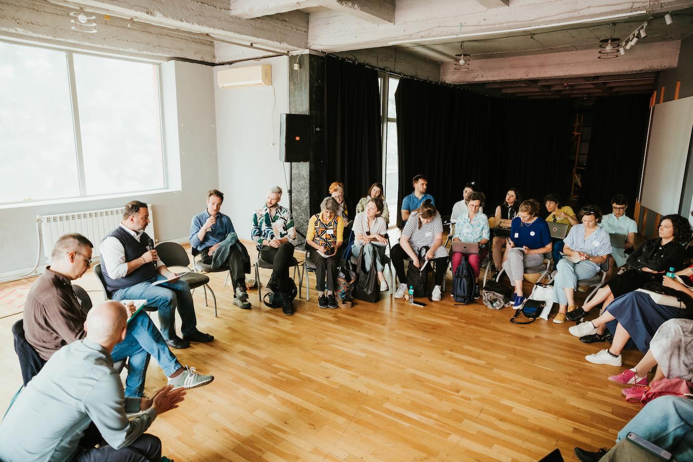 20+ people sitting in a circle, one of them talking into a mic.
