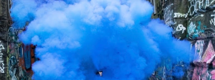 A blooming cloud of bright blue smoke in between two graffitied walls.