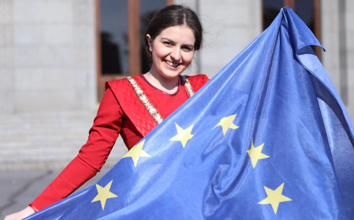 A woman smiles while holding up a large EU flag.