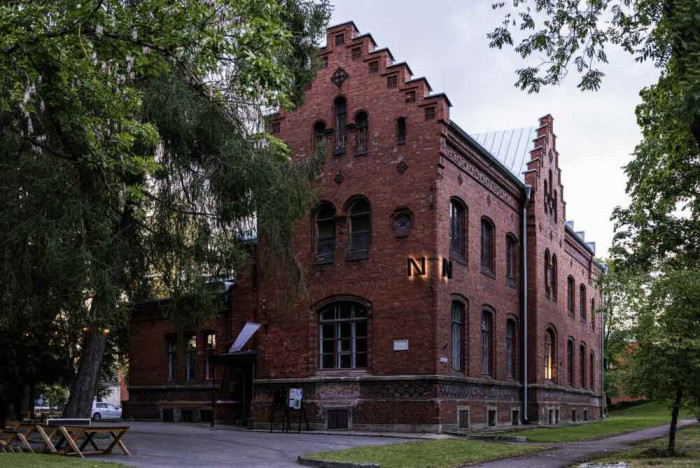 A three story red brick building in a classical style amongst trees.