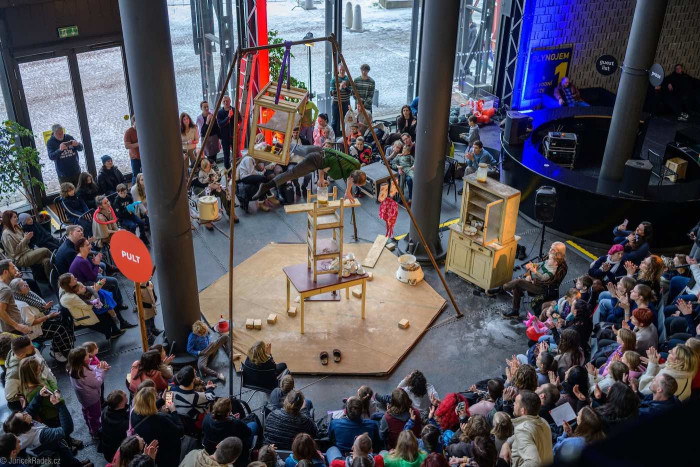 People performing on objects surrounded by an audience, in an indoor space. 