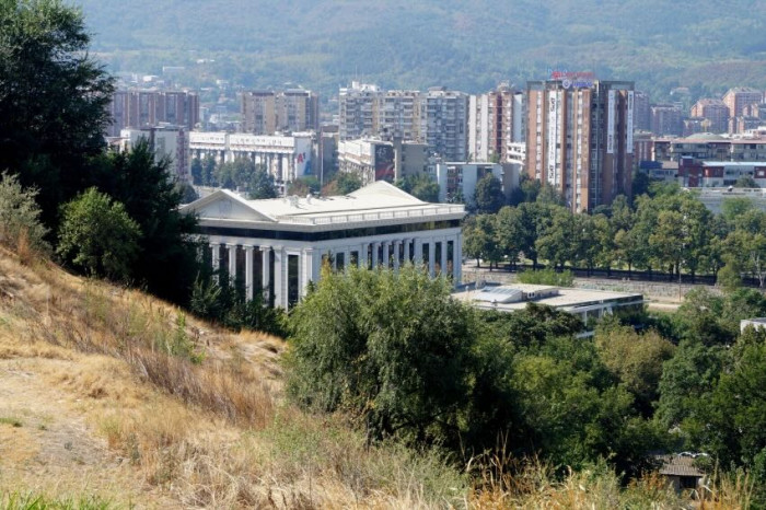 A hill, a classical building and behind the view of a city. 