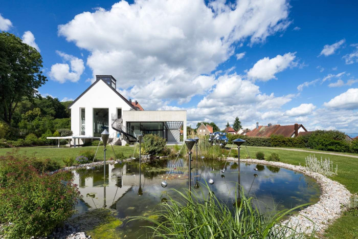 A white, one-story building surrounded by a landscaped garden with a pond and sculptures. 