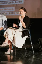 A person sitting on stage talking in a microphone. 