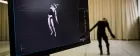 An animated robot on screen hits a dancerly pose. Behind the screen a dancer decked out in mocap gear holds the same position - the animation is a live feed.