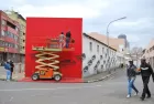 Two men standing on top of a platform, working on a very red mural in a residential street.