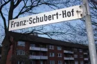 An Austrian street sign reads 'Franz-Schubert-Hof'. In the background is a row of terraced houses.