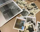 A pile of old black and white and monochrome photographs on a wooden desk.