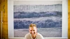 A smiling man in front of a large print of rolling ocean waves.