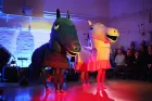Two big, grinning pantomime horses - one pink, one black - stand in a small performance space with audience seated around.
