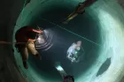A man is abseiling down an incredibly long concrete pipe. Below him is a spherical floating robot thing, like a space probe.