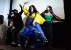A singer or rapper with a mic and two dancers bust some moves on stage.