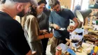 A small group of makers clustered around a workbench filled with tools and blocks of wood in various sizes.