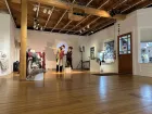 Two people in a gallery exhibition, handling an object that looks like a puppet. 