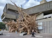 A wooden installation outside an industrial-type cement building. 
