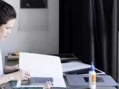 A person working at a table facing a window. 