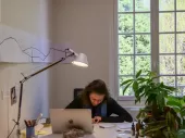 A person working at their desk with a window behind them. 