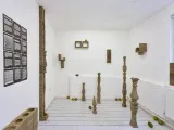 A gallery space with works on the walls and sculptural pieces in the middle. 