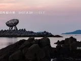 Title of the call on a photo of an artwork perched on rocks beside the sea. 