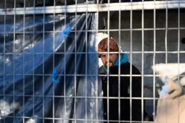 A man, a refugee, is seen through the barrier of steel fencing.