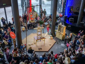 People performing on objects surrounded by an audience, in an indoor space. 