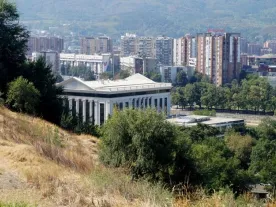 A hill, a classical building and behind the view of a city. 