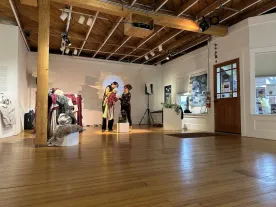 Two people in a gallery exhibition, handling an object that looks like a puppet. 